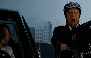  Gernot Hassknecht sitzt auf einem Fahrrad und radelt geradewegs auf eine sich öffnende Autotür zu. Er trägt einen Helm. 
