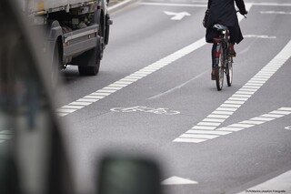 Ein Radfahrer fährt auf einem Schutzstreifen, der geradeaus führt und sich nach rechts verzweigt. Links von ihm fährt ein Lkw. 