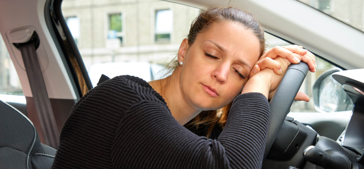 Eine Frau schläft auf dem Lenkrad eines Autos.