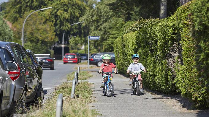 Zwei Kinder im Kitaalter fahren auf einem Gehweg