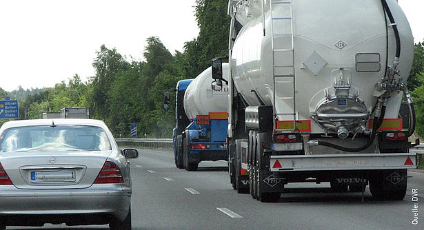 Beim Überholen von Lkw muss ausreichend Platz gelassen werden, bevor wieder eingeschert wird. Ein grauer Pkw setzt zum Überholen von zwei Lkws an, die hintereinander fahren. Es ist ein sonniger Tag.