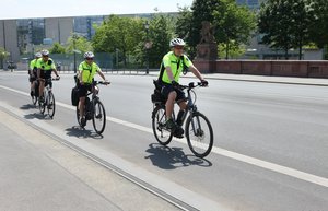 Drei Menschen mit Fahrradhelm und gelber Warnweste fahren hintereinander Fahrrad