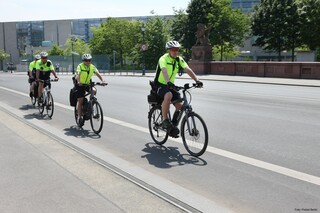 Drei Menschen mit Fahrradhelm und gelber Warnweste fahren hintereinander Fahrrad