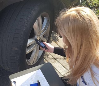 Eine Frau mit blonden langen Haaren kniet neben einem Reifen und misst den Druck mithilfe eines elektronischen Geräts. Foto: DVR