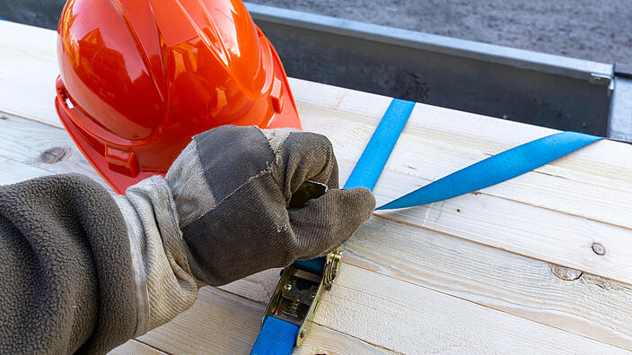 Construction worker secures load on a car trailer with tension straps