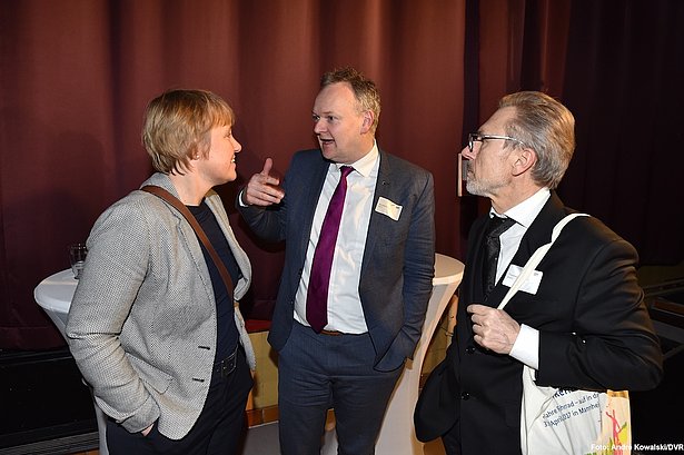 v.l.n.r.: Karola Lambeck, Radverkehrsbeauftragte BMVI, ADFC-Bundesgeschäftsführer Burkhard Stork, Thomas Hartmann, Rad- und Fußverkehr BMVI. Vor einem roten Vorhang stehen zwei Männer und eine Frau. Sie unterhalten sich angeregt miteinander.