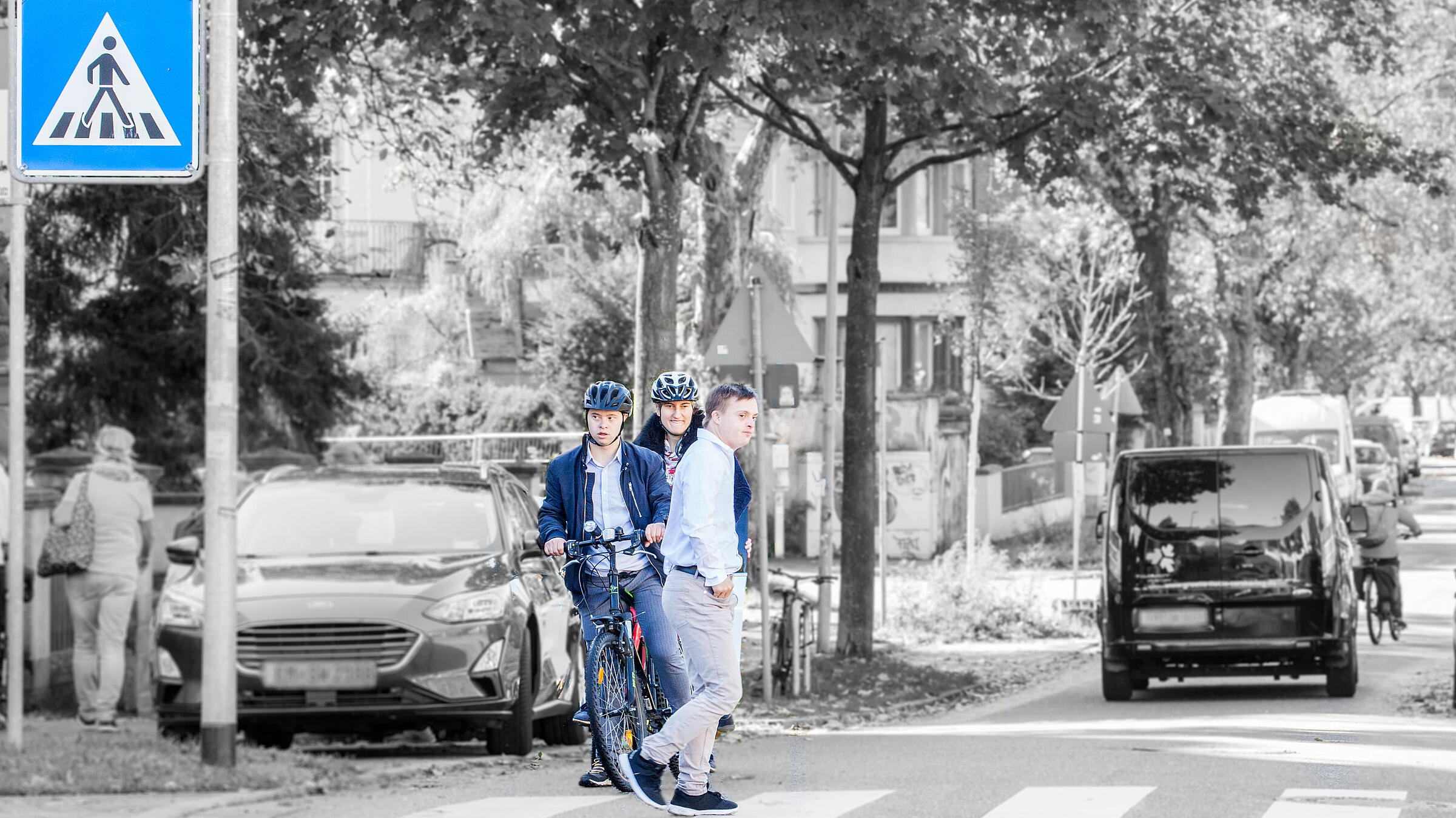 Zwei Fahrradfahrer warten an einem Zebrastreifen, während ein Mann die Straße quert.