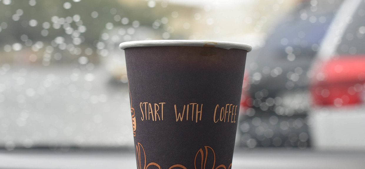 Kaffee hilft nicht gegen akute Müdigkeit beim Autofahren. Foto: Unsplash Ein Kaffeebecher steht auf einer Autofront.