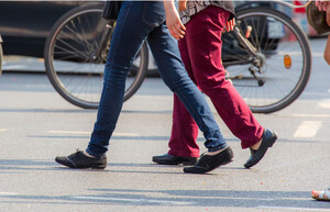 Drei Menschen überqueren eine Straße von rechts nach links. Man sieht nur ihre Beine und Füße.