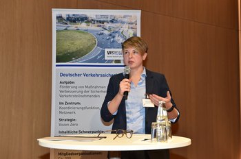 Jessica Niester Eine Frau steht mit einem Mikrofon hinter einem Stehpult