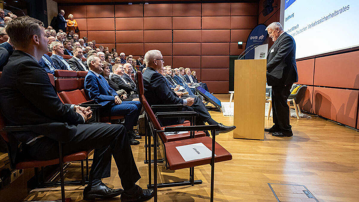 Manfred Wirsch begrüßt am Redepult die Gäste. Die Ränge sind voll besetzt.