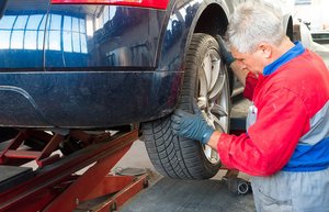 Ein blaues Auto ist auf einer Hebebühne. Ein Mann mit Handschuhen setzt den hinteren Autoreifen an.