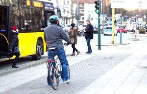Radfahrer fährt auf dem Radweg neben einem gelben Bus. Vor ihm steigen Menschen in den Bus
