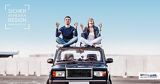 Ein junger Mann und eine junge Frau sitzen auf dem Dach eines Geländewagen und lachen.