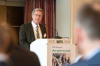 DVR-Präsident Prof. Dr. Walter Eichendorf steht auf dem Podium hinter einem Pult. Die Aufnahme ist aus der Perspektive des auf Stühlen sitzenden Publikums gemacht.