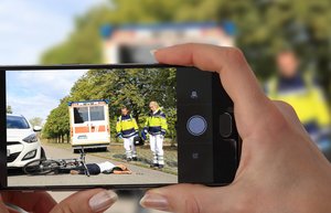 Frauenhände halten ein Smartphone. Im Bild sieht man einen Unfall.
