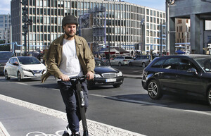 Ein Mann fährt mit einem E-Scooter auf einem Radweg. Er trägt einen Helm.