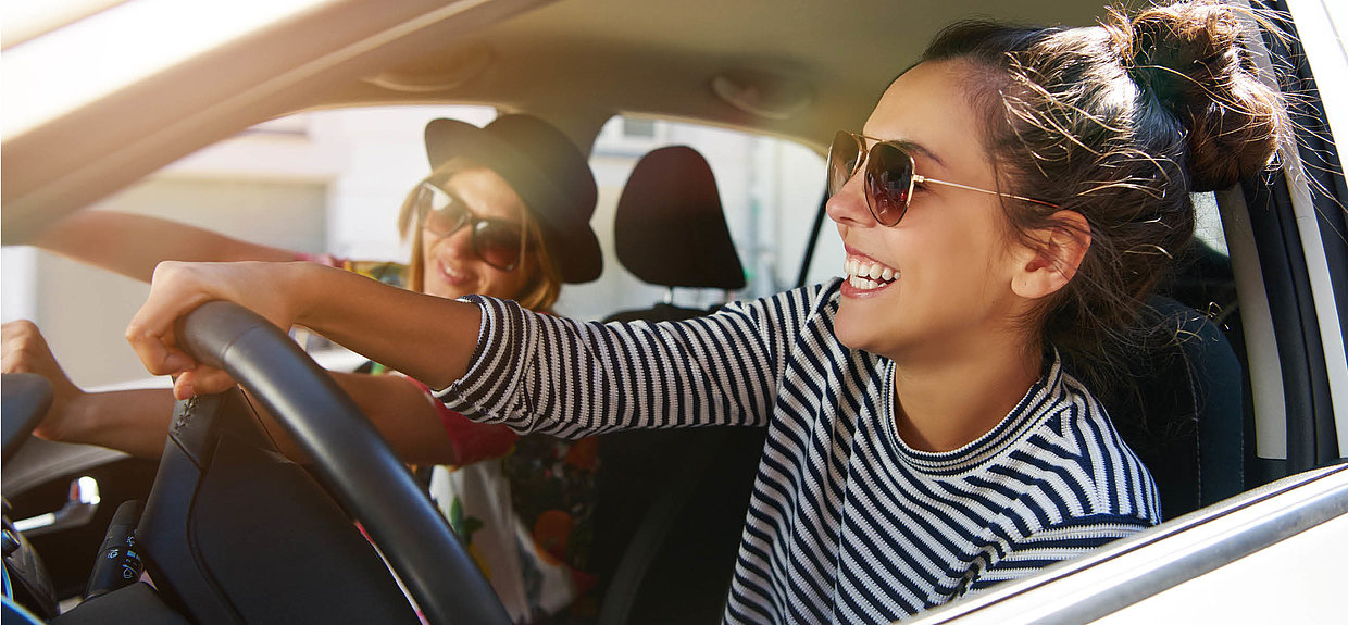 Zwei junge Frauen lachend im Auto.