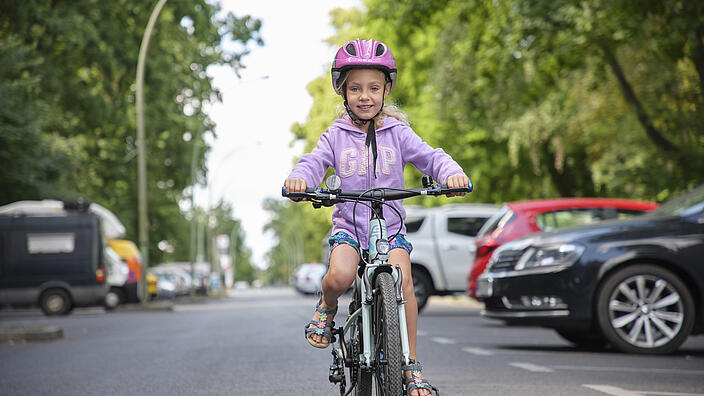 Ein Mädchen fährt auf einem Fahrrad. Sie trägt einen rosa Helm.