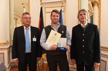 Mathias Kaeser, Foto: Tino Lex Drei Männer stehen nebeneinander, der mittlere hält eine Urkunde