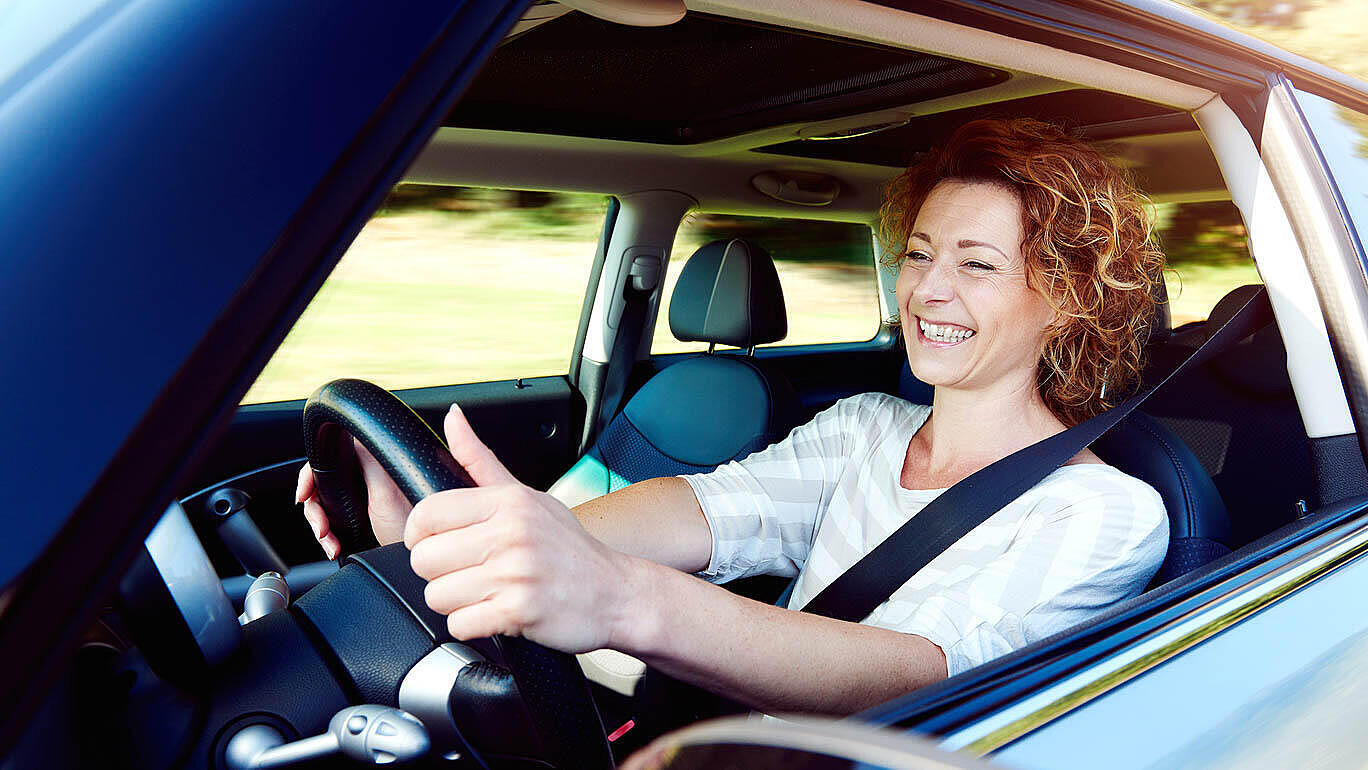 Happy female driver steering car with safety belt