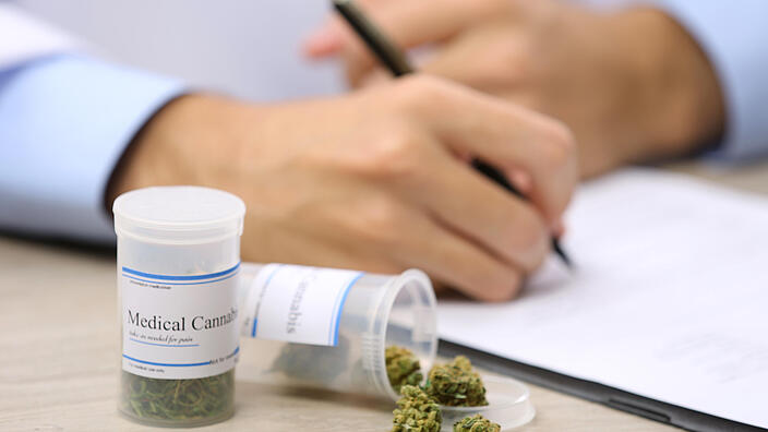 Doctor writing on prescription blank and bottle with medical cannabis on table close up