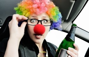 Eine Frau mit bunter Haarperücke hält eine grüne Flasche in der Hand.