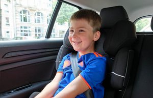 Ein Junge im Grundschulalter sitzt in einem Kindersitz auf der Rückbank eines Autos.