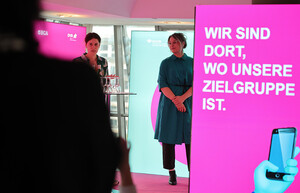 Zwei Personen auf der Bühne, im Vordergrund ein rosa Hintergrund mit dem Text „Wir sind dort, wo unsere Zielgruppe ist“