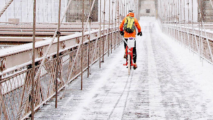 Ein Fahrradfahrer fährt über eine schneebedeckte Brücke.