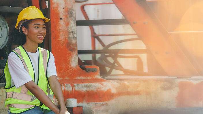 Portrait of happy african american woman dock worker smiling and sitting take a break looking up to dream in factory outside