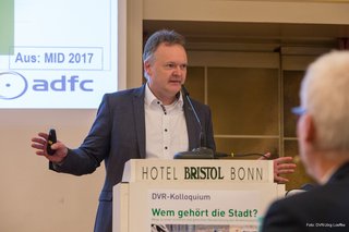 Burkhard Stork, Geschäftsführer des Allgemeinen Deutschen Fahrradclubs (ADFC), steht hinter dem Rednerpult. Die Kamera lichtet ihn frontal ab. 