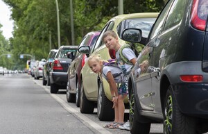 Ein Junge und ein Mädchen im Alter von sechs Jahren schauen zwischen parkenden Autos hervor.