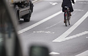 Ein Radfahrer fährt auf einem Schutzstreifen, der geradeaus führt und sich nach rechts verzweigt. Links von ihm fährt ein Lkw. 