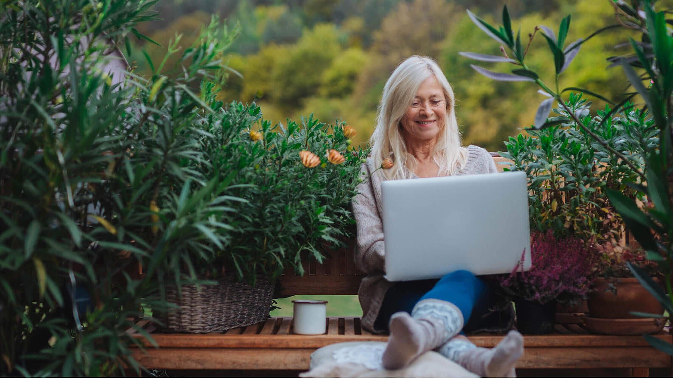 Older woman working from homeoffice, sitting on terrace with laptop.