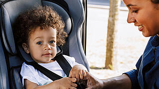 Mother fastening her little son safely in a car seat