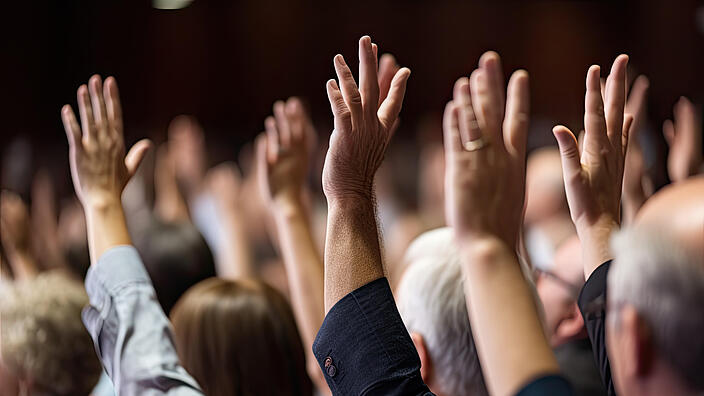 A diverse audience raises their hands in an important decision.