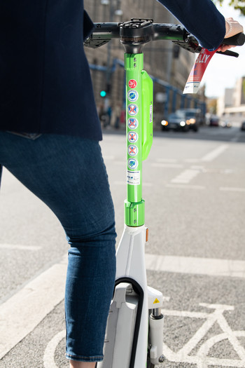 Eine Frau steht fährt mit einem E-Scooter, es ist nur ihr Bein und ihr Arm von hinten zu sehen