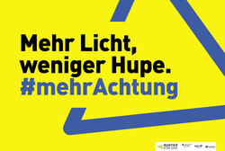 Gelber Hintergrund mit blauem Warndreieck, dazu der Text: Mehr Licht, weniger Hupe. #MehrAchtung