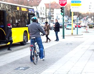 Radfahrer fährt auf dem Radweg neben einem gelben Bus. Vor ihm steigen Menschen in den Bus