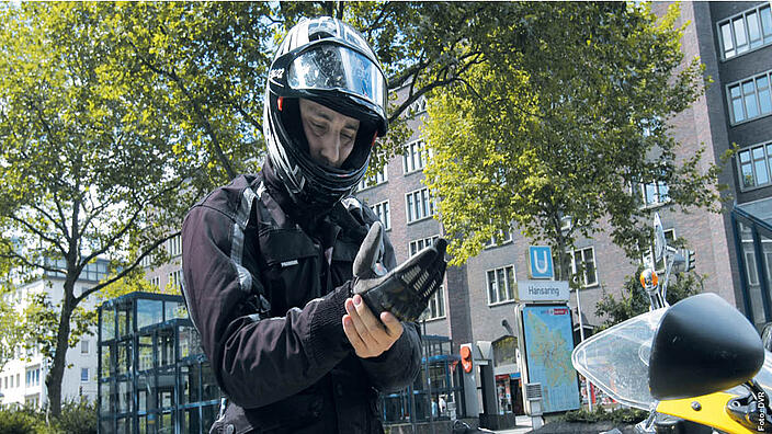 Mann stehend vor Motorrad in Motorradkleidung während er seinen Handschuh anzieht