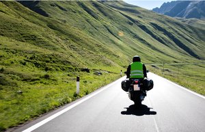 Ein Motorradfahrer fährt auf einer Landstraße durch die Berge. Die Sonne scheint.