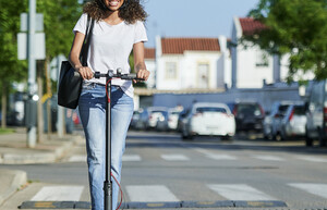 Eine Frau fährt mit einem E-Scooter auf der Straße. Dabei trägt sie einen Helm.