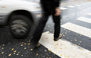 Eine Person geht über den Zebrastreifen. Ein Auto naht mit erhöhter Geschwindigkeit. Es ist leicht verwischt.