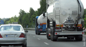 Ein grauer Pkw setzt zum Überholen von zwei Lkws an, die hintereinander fahren. Es ist ein sonniger Tag. 