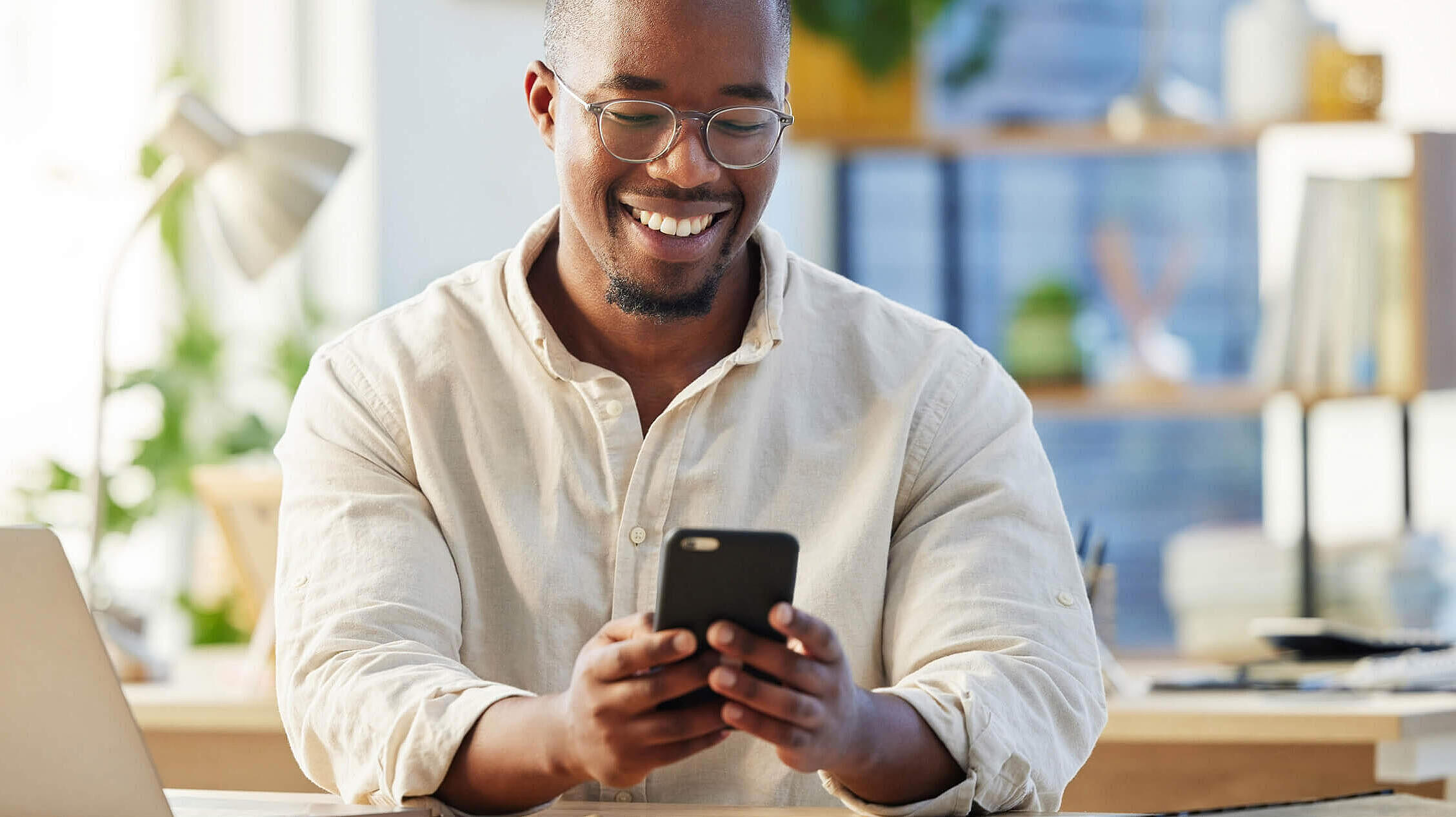 African business man, texting and phone in office with smile, connection and meme on social media app. Happy black businessman, typing and smartphone for networking, contact and reading blog on web