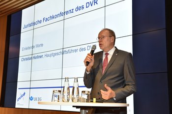 Ein Mann steht mit einem Mikrofon vor einer Leinwand