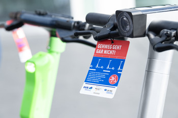 Am Lenker eines E-Scooters hängt ein Flyer der Kampagne Roll ohne Risiko