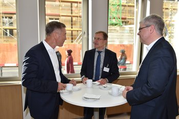 Drei Männer stehen an einem Stehtisch