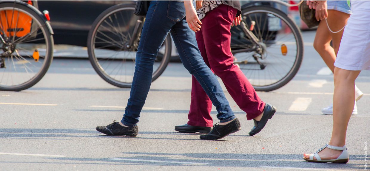 Fußgänger und Fußgängerinnen überqueren eine Straße. Foto: Adobe Stock Drei Menschen überqueren eine Straße von rechts nach links. Man sieht nur ihre Beine und Füße.